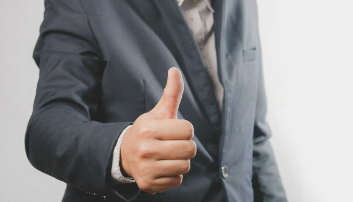 Close up of a businessman in a suit with a thumb up standing. Do