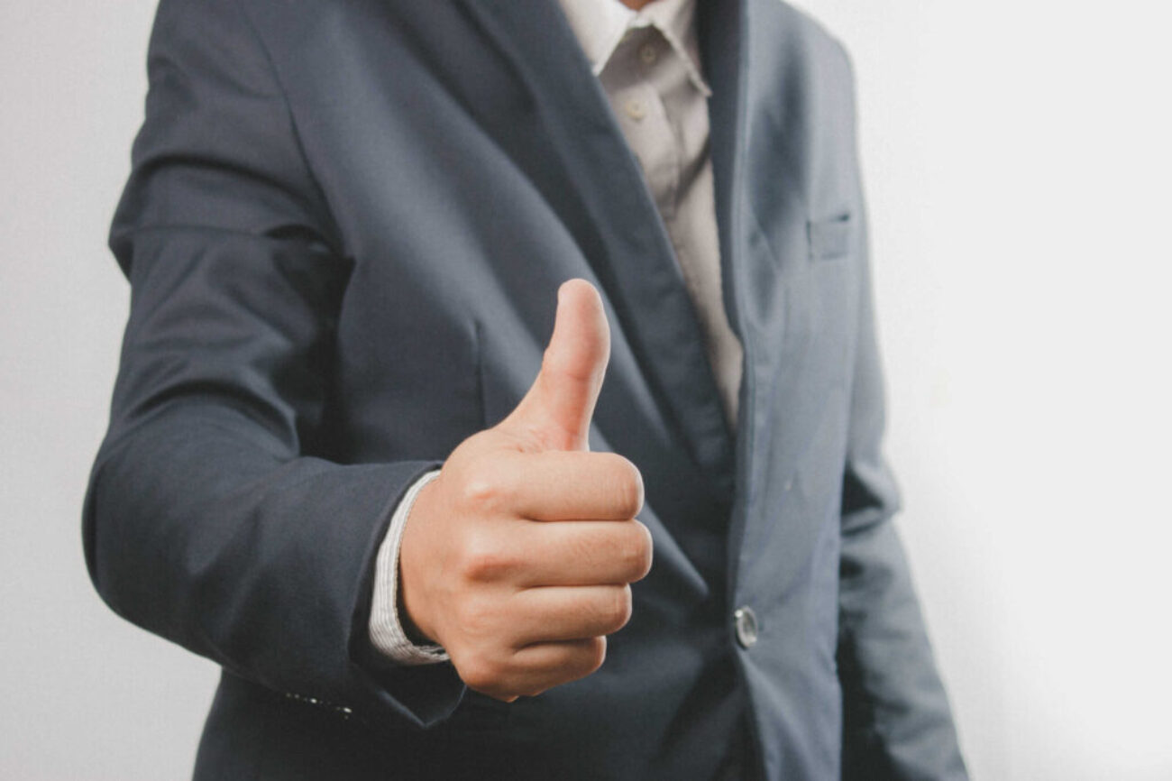 Close up of a businessman in a suit with a thumb up standing. Do