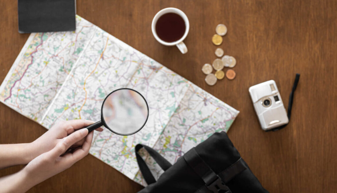 Flat lay, travel planning, trip, map and magnifying glass in female hands.