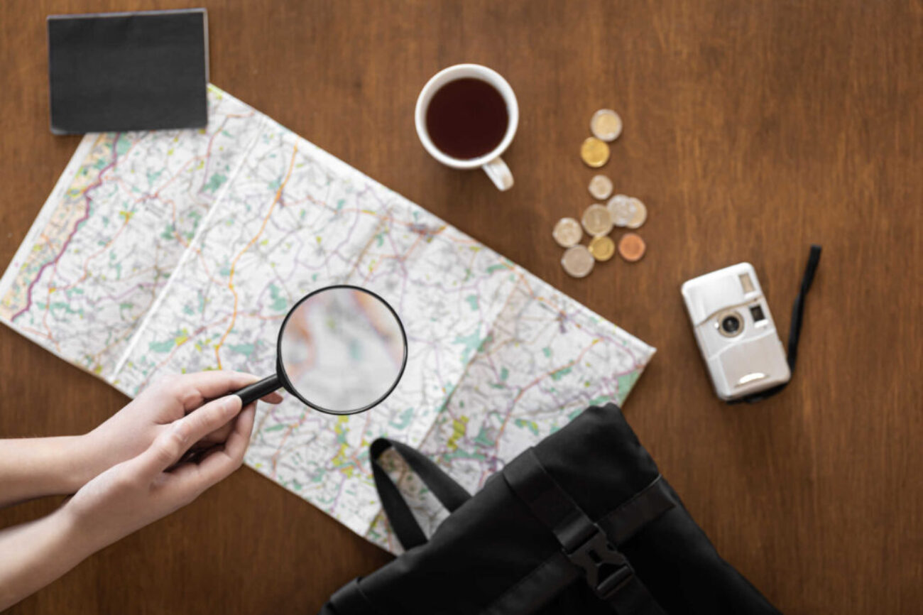 Flat lay, travel planning, trip, map and magnifying glass in female hands.