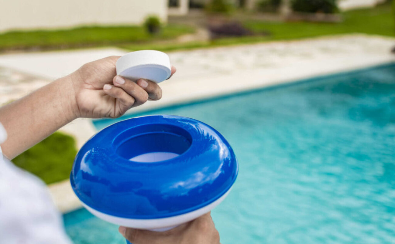 Hands holding a dispenser with pool chlorine tablet, pool float and chlorine tablets for pool maintenance. Hands holding a pool chlorine dispenser. Hand of a pool disinfection worker holding a dispenser with a chlorine tablet.