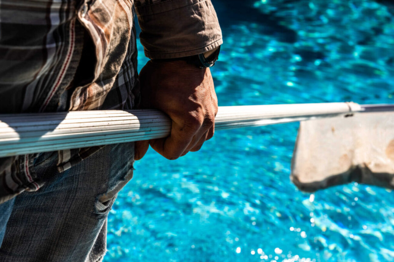 Maintenance man using a pool net leaf skimmer rake in summer to