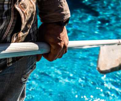 Maintenance man using a pool net leaf skimmer rake in summer to