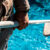 Maintenance man using a pool net leaf skimmer rake in summer to