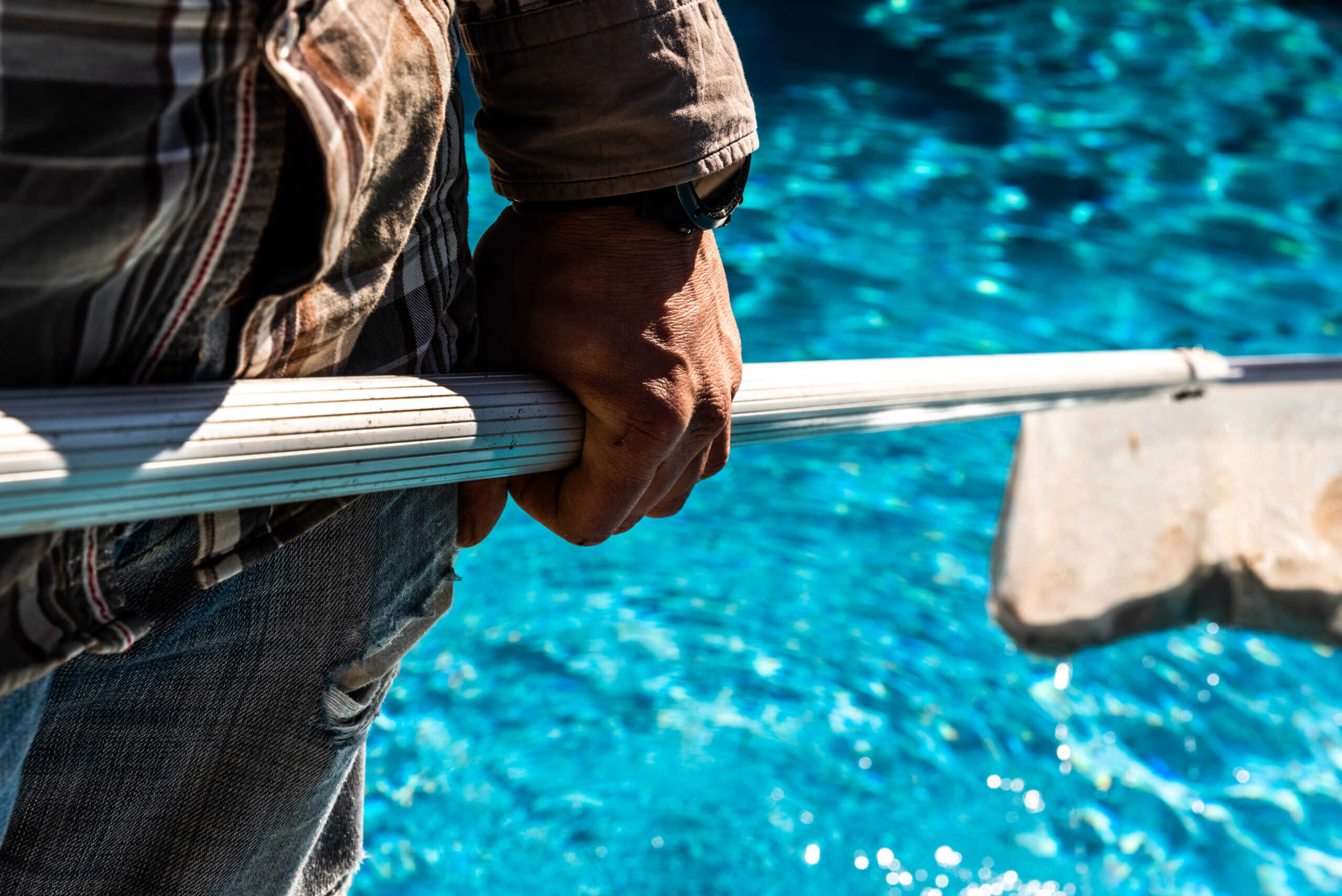 Maintenance man using a pool net leaf skimmer rake in summer to