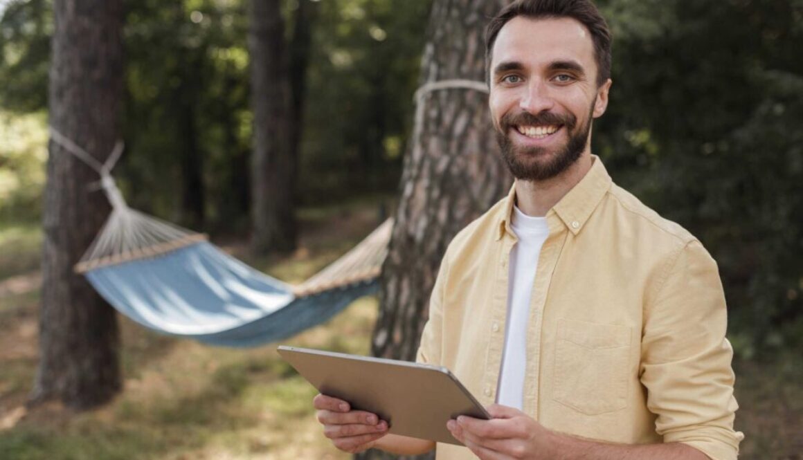 smiley-man-holding-tablet-while-camping-outdoors