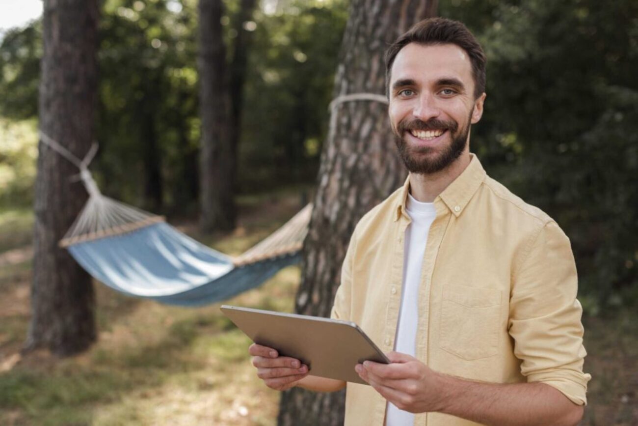 smiley-man-holding-tablet-while-camping-outdoors