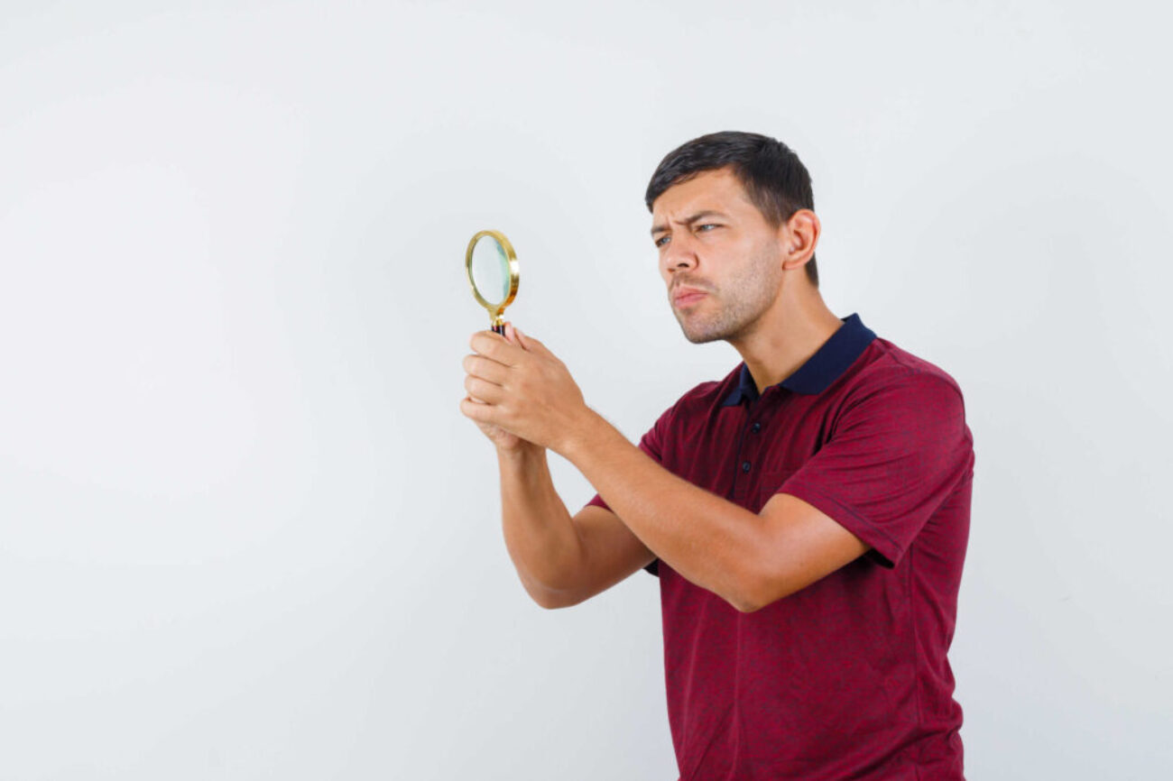 Young man looking through magnifying glass in t-shirt front view.