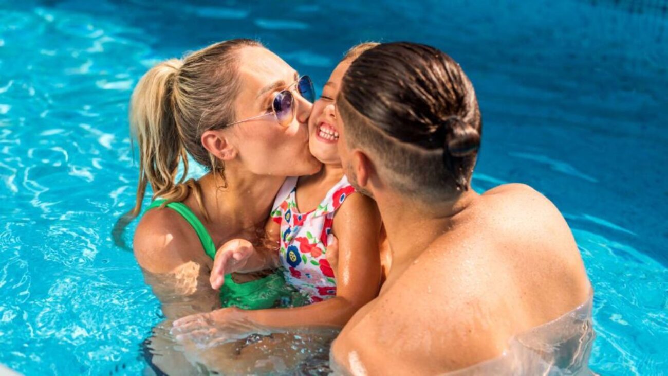 happy-parents-kissing-their-smiling-daughter-while-swimming-pool_0x800