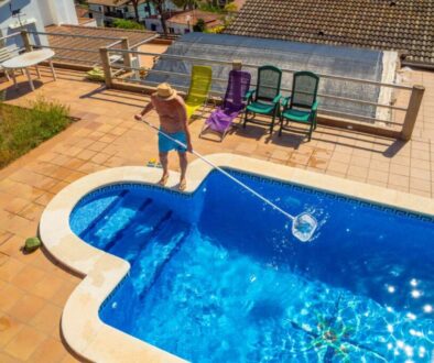 man-with-straw-hat-dressed-swimming-trunks-cleaning-his-pool-with-pool-cleaner-stick-from-leaf_0x800