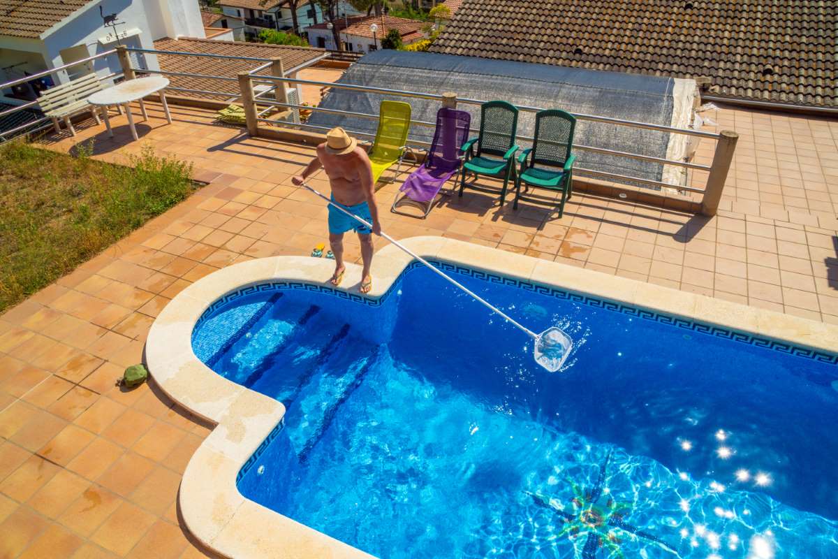 man-with-straw-hat-dressed-swimming-trunks-cleaning-his-pool-with-pool-cleaner-stick-from-leaf_0x800