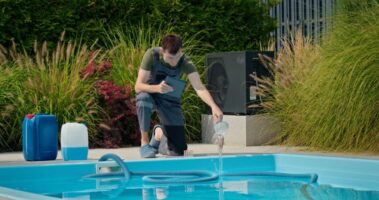 pool-technician-pouring-liquid-into-pool-while-using-tablet-surrounded-by-chemical-containers_0x800