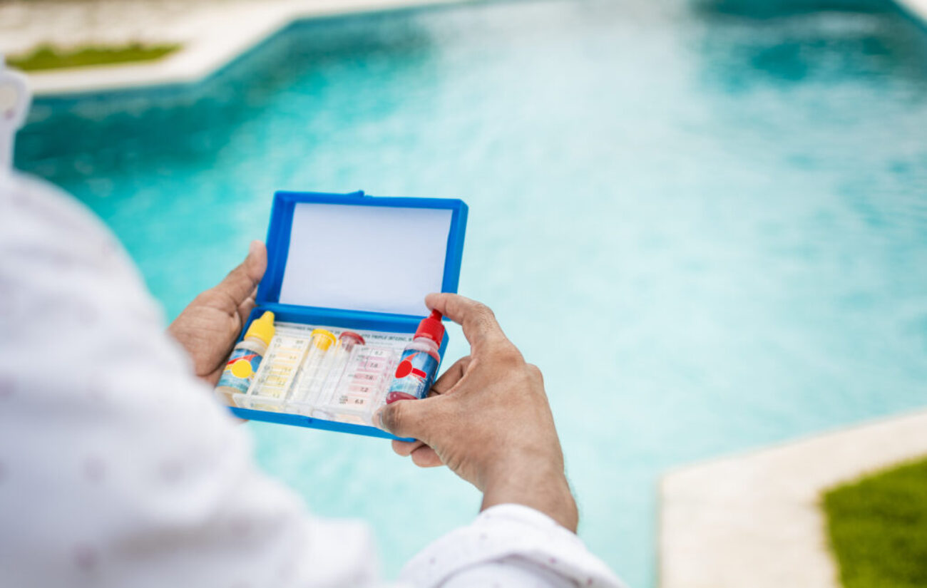 Hand holding Water Test Kit on blurred pool background, Hand holding a pool ph and chlorine tester, Person holding complete water test kit with blurred pool background