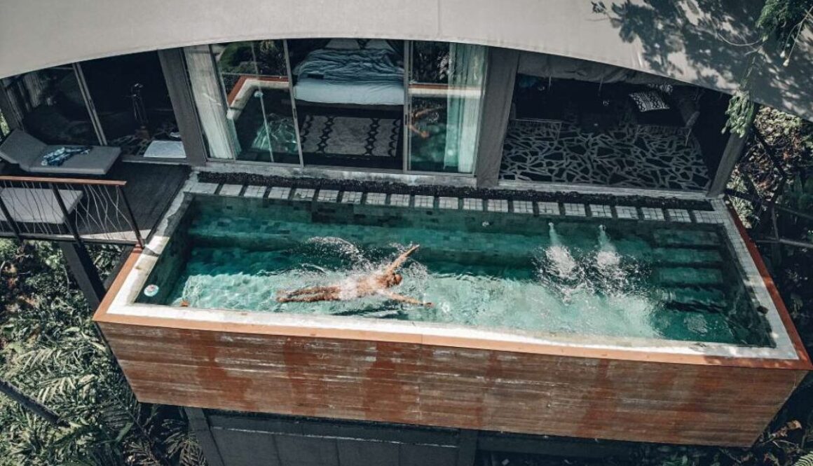 aerial-view-fit-male-swimming-clear-pool-that-is-balcony-hotel-palms-around-arched-grey-roof-recreation-concept_0x800