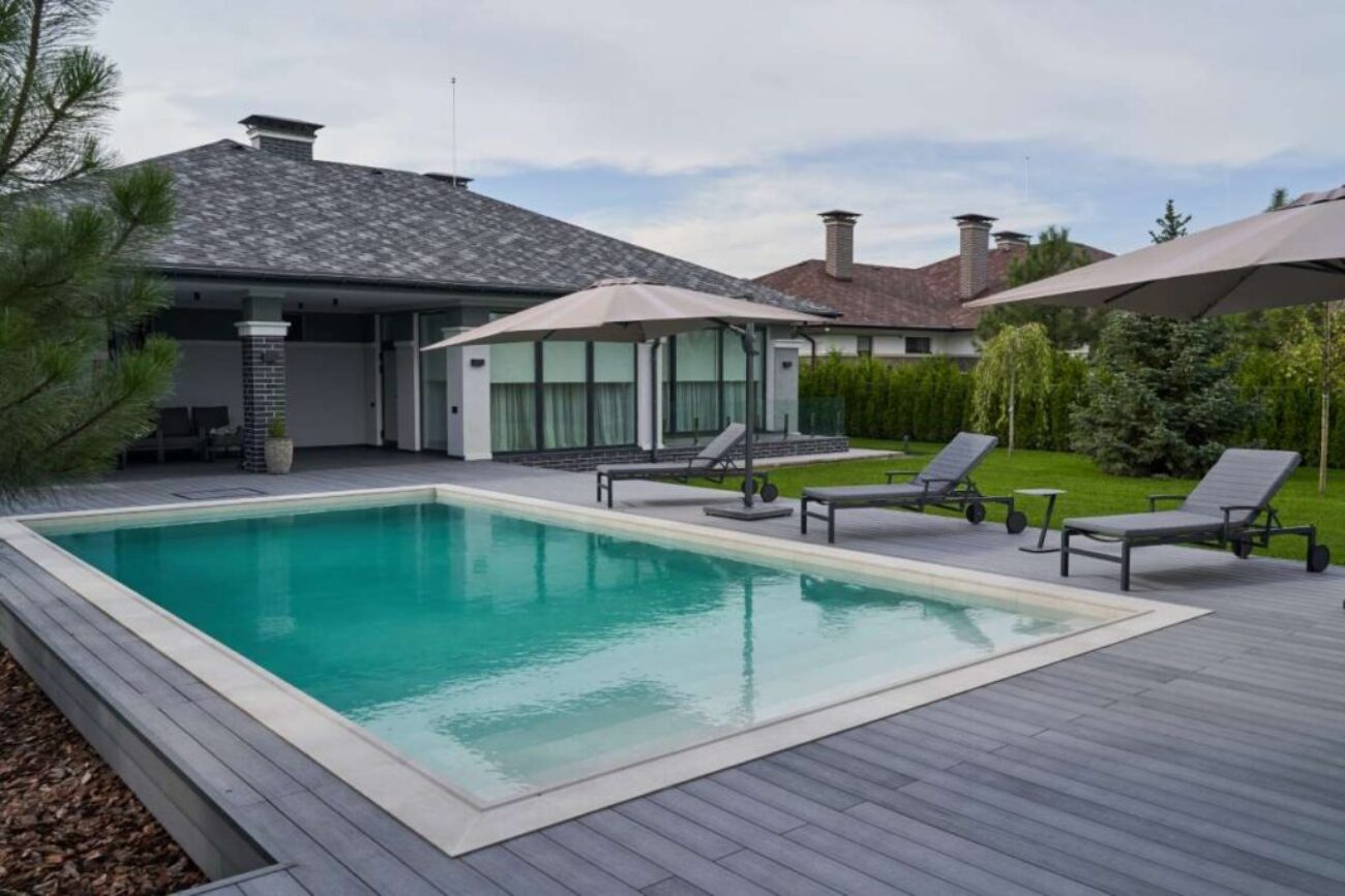 wooden-lounge-chairs-modern-villa-pool-deck-light-blue-water-swimming-pool-luxurious-mansion-with-chairs-around-it-modern-house-background_0x800