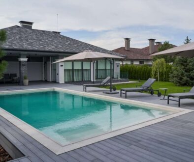 wooden-lounge-chairs-modern-villa-pool-deck-light-blue-water-swimming-pool-luxurious-mansion-with-chairs-around-it-modern-house-background_0x800